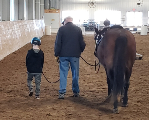 Volunteer, student, and horse walk together through arena.