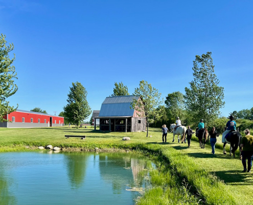 Participants ride horses beside the pond on a spring evening.